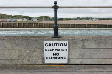 A sign saying, Caution Deep Water No climbing, on a handrail next to fast flowing water visible in backgroundの写真素材