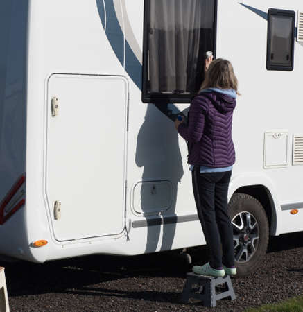 A lady motorhome owner cleans her recreational vehicle window.She stands on a step to reach the window.RVの写真素材