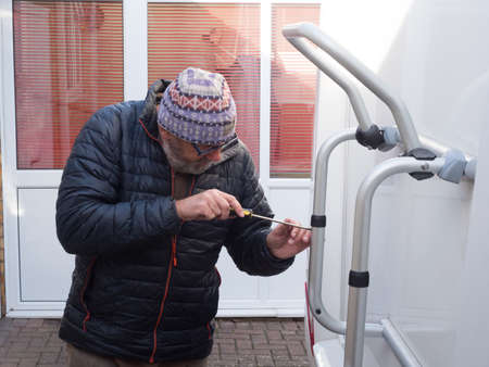 A man uses a screwdriver to work on his rear bike rack of his motorhome recreational vehicle. He wears a hat and glassesの写真素材
