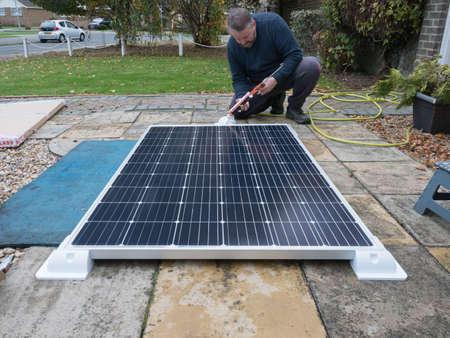 A man kneeling can be seen using a sealant gun with a large motorhome recreational vehicle solar panel on the ground in front of him._の写真素材
