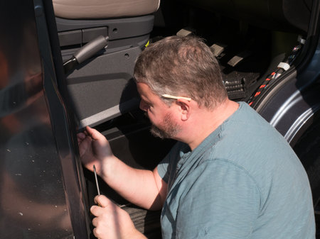 A male bearded mechanic works in the front cab footwell of a motorhome recreational vehicle.He has a pencil behind an ear and screwdriver in handの写真素材