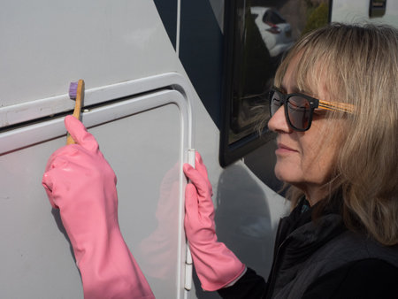 An attractive lady hand cleans her motorhome recreational vehicle with a toothbrush. She wears pink rubber gloves and sunglasses.の写真素材