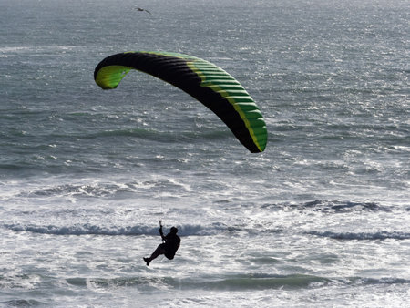 A paraglider flies above an ocean with waves.Backlit silhouette