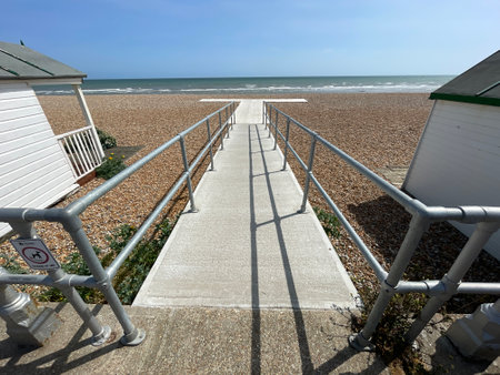 A concrete ramp with railings runs out onto a pebble beach to allow disabled wheelchair users access to an area to view the sea.Ocean in background.Blue sky day.Equality.の写真素材