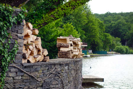 Cut firewood lies on a stone wall by the lakeの写真素材
