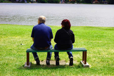 Retired couple sit on a bench by the lake and relaxの写真素材