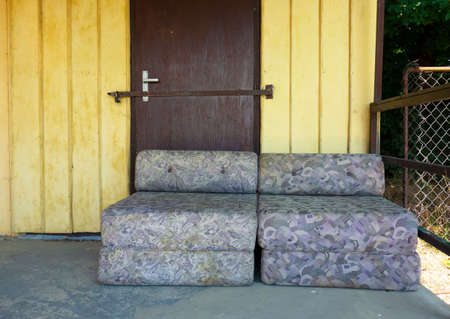 An old couch stands in front of the locked door of an abandoned natural hostel