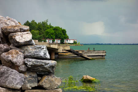 Harbor pier made of concrete and wood on the lake by a wall of stone, in the background above the horizon are active storm cloudsの写真素材