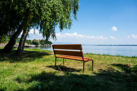 Wooden bench on the grassy beach of a recreational destination by the lake in the parkの写真素材