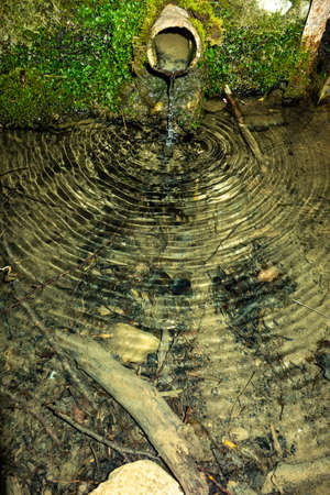 A stream of running water from a forest well creates water ripples at the surface of the lake