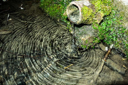 A stream of running water from a forest well creates water ripples at the surface of the lake