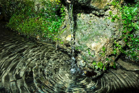 A stream of running water from a forest well creates water ripples at the surface of the lake