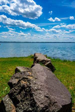 Large rocks on the grassy beach by the lake as a barrier against the passage of cars into the restricted zoneの写真素材