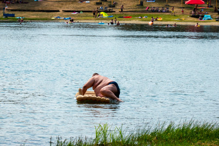 An obese man tries to climb out on an air mattress on a lakeの写真素材
