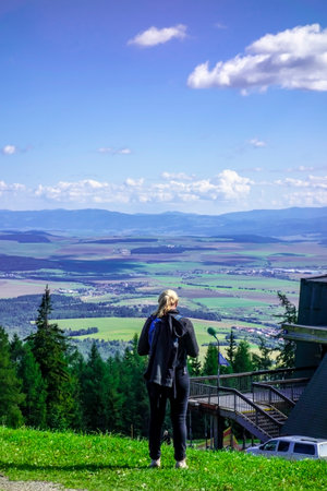 A young woman stands on a hill of the High Tatras and observes the beautiful natural surroundings