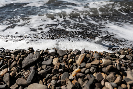 Tidal sea waves with foam on a gravel beachの写真素材