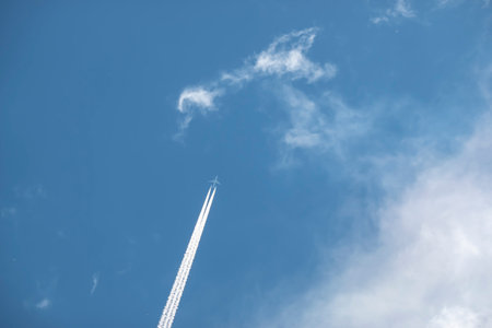A flying plane in the sky leaves a white trail behindの写真素材