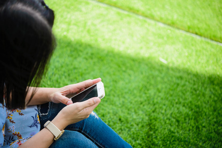 Young girl sitting on green grass with mobile phone.woman using her Mobile Phone. female student...