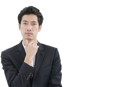 A thoughtful man in black suit with hand on chin looking at camera, isolated on white background, confident and serious expressionの素材