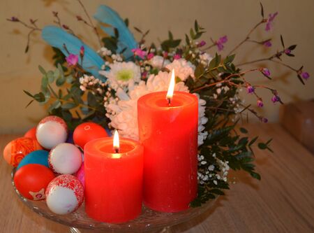 Red festive candles with decorated eggs and flowers in a vaseの写真素材