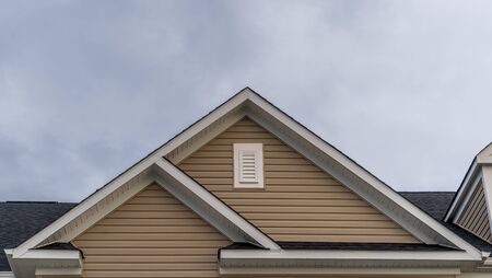 White attic gable vent louver ,white square window,  triangle with red brick or gray beige horizontal lap vinyl siding on a new construction luxury American single family home in the East Coast USAの写真素材
