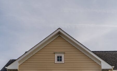 Single gable close up with beige vinyl siding on luxury single family residential home with single attic window in white frame with neutral sky backgroundの写真素材