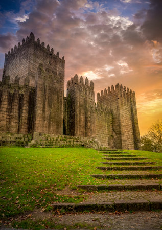 Aerial view of well-preserved medieval buildings hilltop, 10th-century GuimarÃ£es Castle with stunning sunset orange red purple skyのeditorial素材