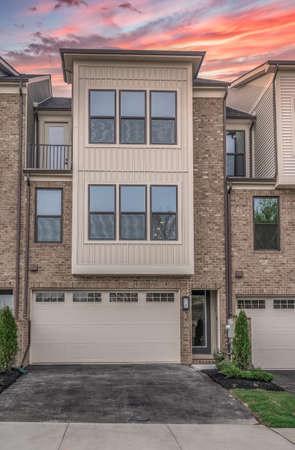 Beautiful new three story townhouse with pop out facade, double car garage, brick front , attic balcony gorgeous colorful orange, blue, red sunset sky at a new real estate development in the USAの写真素材