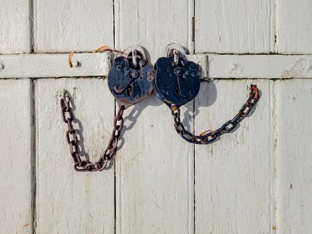 Rustic metal locks with chain on a white wooden doorの写真素材