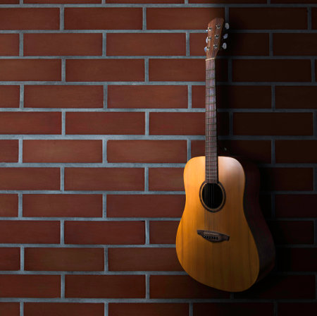 brown acoustic guitar stand in front of brick wall background. Guitar body part front made with top solid, side and back mahogany wood.の写真素材