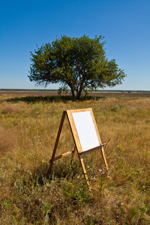 wooden easel stands in a field with a white sheet of paperの写真素材