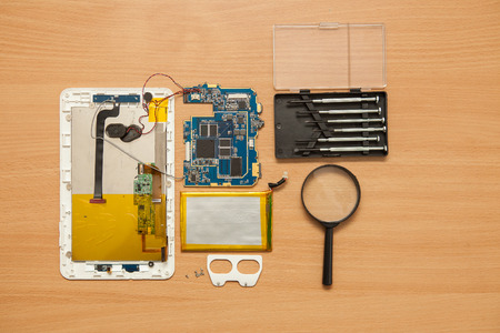 Disassembled tablet and tools on a wooden background. View from above.