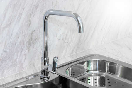Close Up Bright Tall Faucet and Stainless Steel Sink on Luxury Marble Floor Backgroundの写真素材