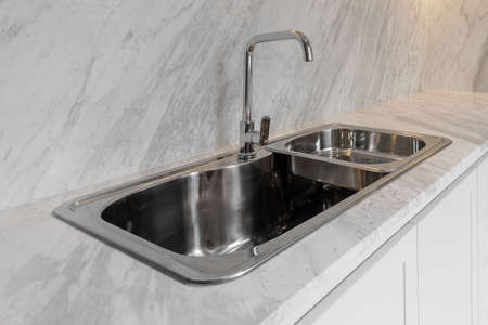 Close Up Bright Tall Faucet and Stainless Steel Sink on Luxury Marble Floor Backgroundの写真素材