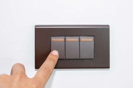 Close up fingers is turning on or turning off the brown light-switch on stenciled white wall.の写真素材