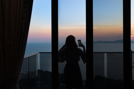 woman taking pictures of sunset at balconyの写真素材