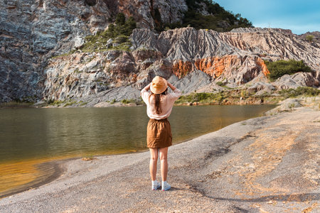 A girl in a hat stands on the shore of a mountain lake.の写真素材
