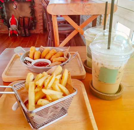 Iced Coffee and French fries on a Wooden Table in a Cozy Coffee Shopの写真素材