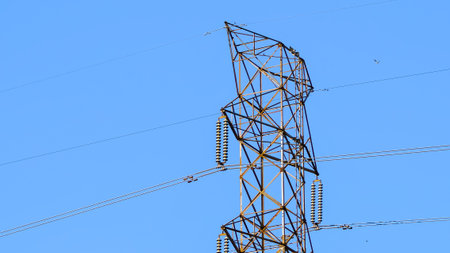 Close-up of high-voltage power poles against a blue sky backdrop.