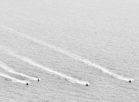 An abstract and graphic monochrome capture from above, showing the sea surface disturbed by the...