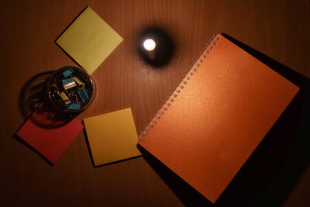 Close-up photos of notebooks and paper clips placed on the table with orange light from candles.の写真素材