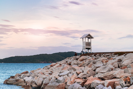 Man with bicycle sitting near life guard house at stone seawall look at sunset sky.の写真素材
