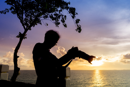 Silhouette man holding camera beside sunset sea.の写真素材