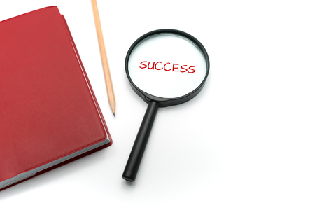 Magnifying glass with word "success" and red cover notebook on white background.の写真素材