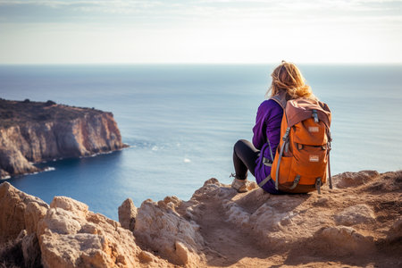 female backpacker sitting on the cliff in front of the seaの素材