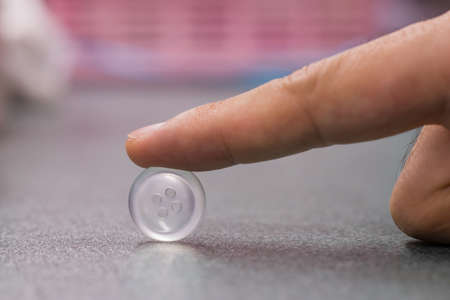 Hand holding a single white button with blurry backgroundの写真素材