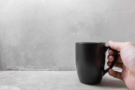 Hand hold black coffee mug on concrete tableの写真素材