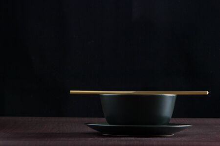 Black bowl with wooden chopsticks on wooden table with black backgroundの写真素材