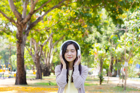 Beautiful asian woman listen to music with white headphone in natural parkの写真素材