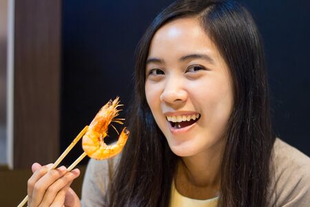 Happy asian woman eating food with chopsticksの写真素材